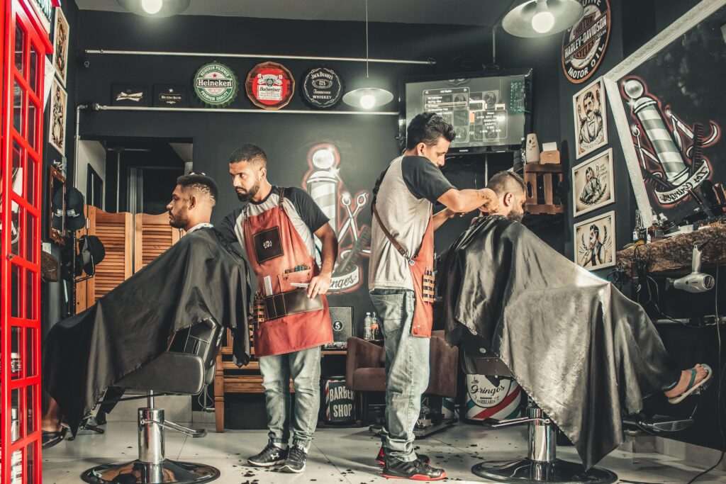 pexels-photo-1813272-1813272 A bustling barbershop with two men getting haircuts, showcasing a vibrant barber environment.