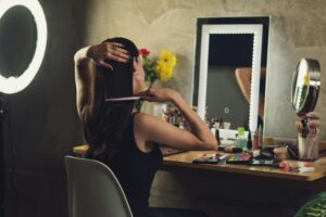 A woman styles her hair at a vanity with a mirror and various cosmetics, creating a personal grooming routine indoors.
